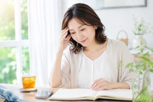 明るい夏の室内で、予定が書かれた手帳を見つめる女性