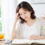 明るい夏の室内で、予定が書かれた手帳を見つめる女性