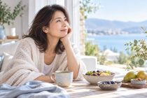 明るい窓辺で朝食を前に穏やかにくつろぐ40〜50代の日本人女性。自分に合った健康習慣を大切にする暮らし。